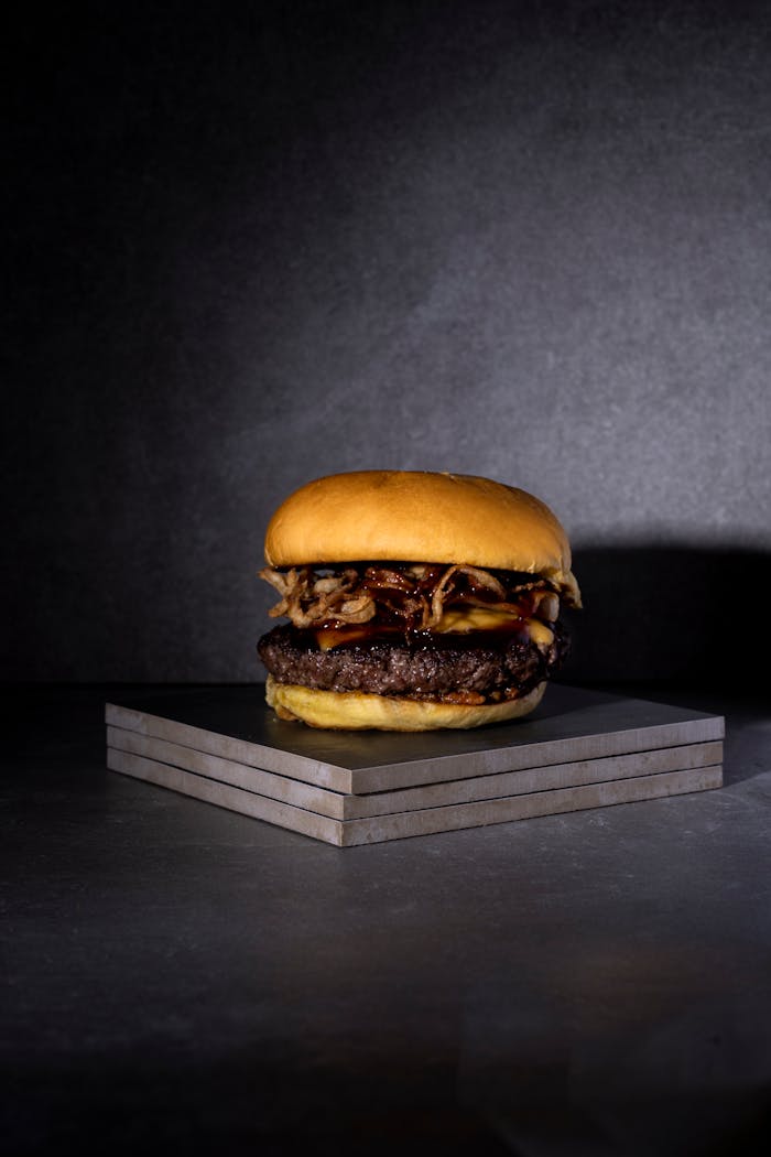 Close-up of a gourmet burger with melted cheese and onions on slate tile surface.
