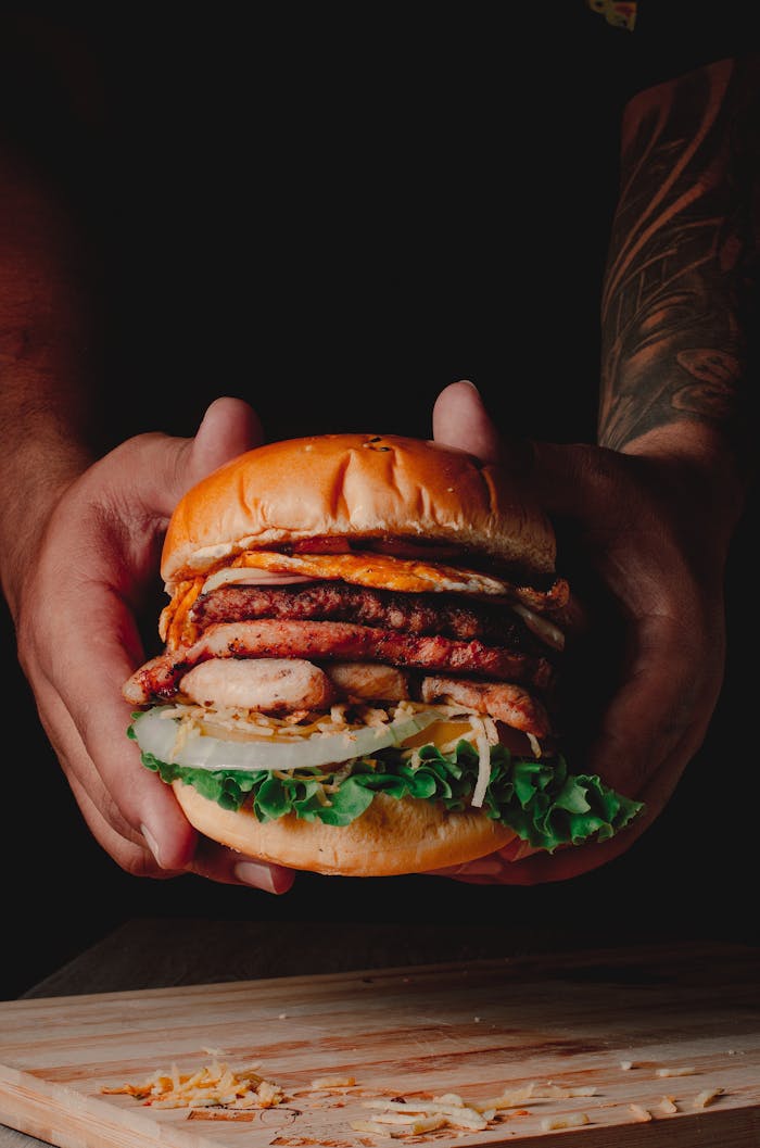 Close-up of a gourmet beef burger with fresh lettuce held by hands above a wooden board.